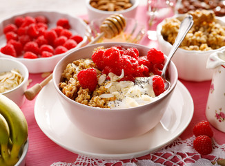 Granola with natural yogurt, raspberries, honey, almond flakes, and poppy seeds in a  bowl on a pink wooden table. A delicious and nutritious breakfast or dessert. Healthy eating concept