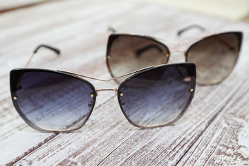 Two pairs of women's stylish sunglasses on white wooden background
