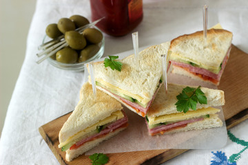 Sandwiches with sausage, meat, cheese and fresh vegetables on a table with olives and ketchup.