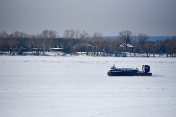 Hovercraft is rushing through a river covered with ice on a clear winter day