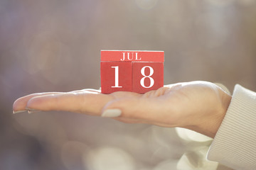 the woman is holding a red wooden calendar. Red wooden cube shape calendar for JUL 18 with hand 