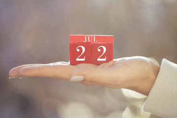 the woman is holding a red wooden calendar. Red wooden cube shape calendar for JUL 22 with hand 