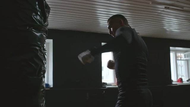 Medium shot of man practicing boxing movements with punching bag when working out at the gym