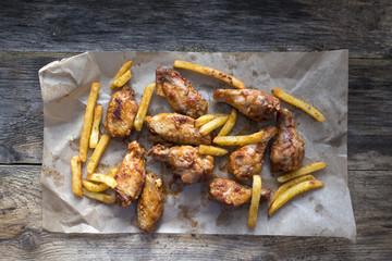 Appetizing fried pieces of chicken, pieces of chicken wings and fried potatoes located on paper and on an old wooden background