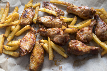 Appetizing fried pieces of chicken, pieces of chicken wings and fried potatoes located on paper and close-up