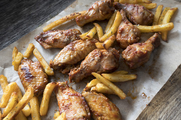 Appetizing fried pieces of chicken, pieces of chicken wings and fried potatoes located on paper and close-up