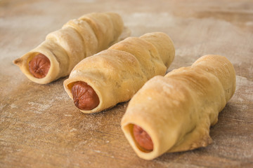 Three sausages in a dough on a wooden background