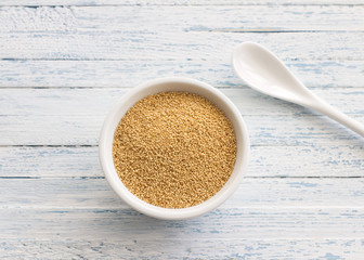 Raw amaranth seeds in a ceramic spoon on a light blue background, top view, selective focus