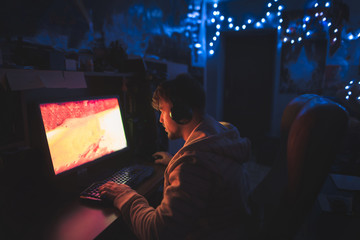 A focused gamer sits at the computer at home in the cozy room and plays horror games on the computer. A man sits at the computer at night and looks at the monitor