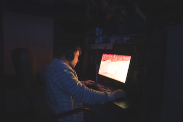 Gamer plays horror games at night at the computer. The man is sitting in a cozy room at the computer and playing the game