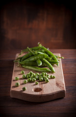 Peas fresh arrangement on wooden cutting board and brown wooden table on dark backgound