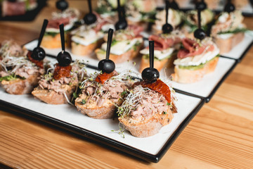 tasty pinchos with tuna, dried tomatoes, olive and pesto sauce, traditional spanish snack, served on a white plate