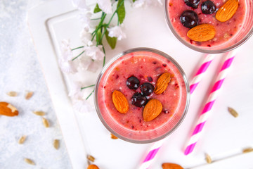 Blueberry smoothies of berries, banana and almonds in glasses with cocktail tubes on a white wooden board.
