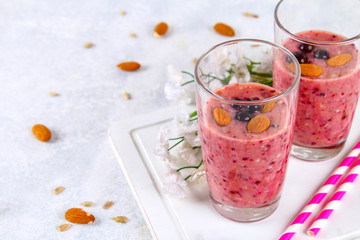 Blueberry smoothies of berries, banana and almonds in glasses with cocktail tubes on a white wooden board.