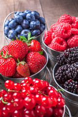 Berries assortment closeup arrangement in tin cans on rustic wooden table in studio