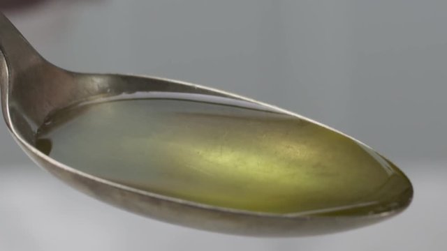 Oil pouring into a vintage tablespoon in the kitchen, shallow focus, slow motion