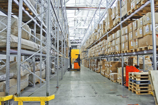 large modern warehouse with forklifts, shelves with pallets, boxes, containers and goods