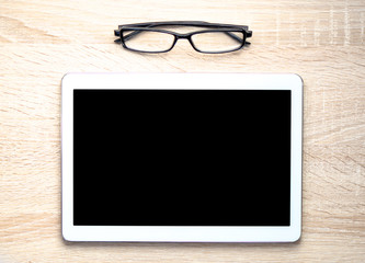 tablet pc with empty screen near glasses on wooden table 