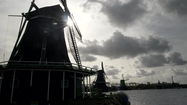 sun shines behind several windmills at zaanse schans near amsterdam, netherlands