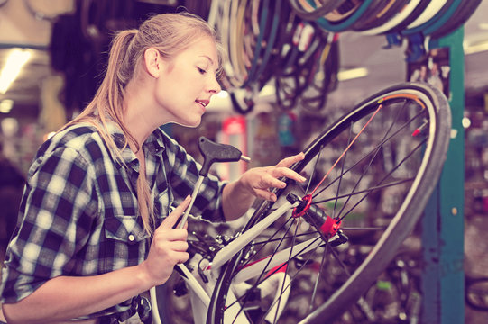 Young woman master repairing wheel of city-bike
