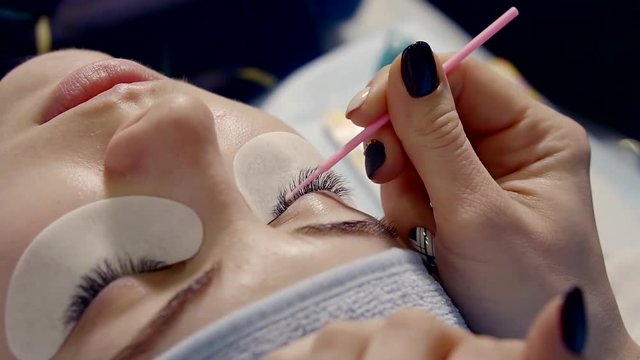 master is preparing client for eyelash extension, leveling eyelashes by plastic tools, woman is lying