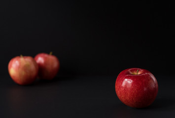 A shiny red apple isolated on black background. Two other apples out of focus in background