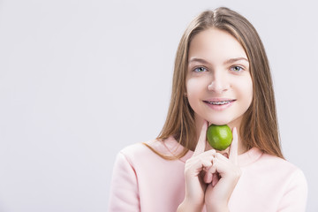 Dental Health Ideas and Concepts. Portrait of Caucasian Teenage Girl with Correcting Teeth Brackets. Posing with Green Small Lime under Chin.