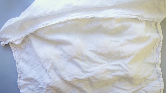 Older woman covers rising dinner rolls with a tea towel in a rustic farmhouse kitchen. The aging baker lets the dough balls rest before baking the homemade bread in the oven.