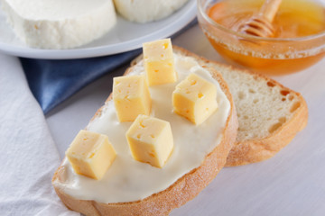 Cheese and honey on a white plate, kefir and sandwich with soft cheese, minimalism, honey and a piece of bread on the blue napkin, French breakfast on a white background, American cuisine