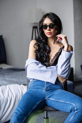 Fototapeta na wymiar portrait of a beautiful brunette in sunglasses, blue shirt, blue jeans and interior in room