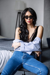 Fototapeta na wymiar portrait of a beautiful brunette in sunglasses, blue shirt, blue jeans and interior in room
