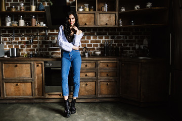 Fototapeta na wymiar Beautiful brunette in the kitchen, modern housewife, fashion, wooden brown furniture, dressed in blue jeans and a blue shirt