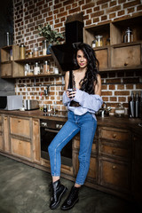 Beautiful brunette in the kitchen, modern housewife, fashion, wooden brown furniture, dressed in blue jeans and a blue shirt