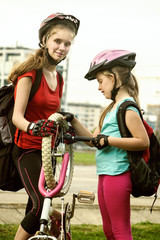 Obraz premium Bicycle tire pumping and repair by child bicyclist. Girl repairing bicycle on road . Kids pump up tire. Children return home from school on bicycles. Tone image. They help children repair bicycles.