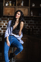Obraz na płótnie Canvas Beautiful brunette in the kitchen, modern housewife, fashion, wooden brown furniture, dressed in blue jeans and a blue shirt