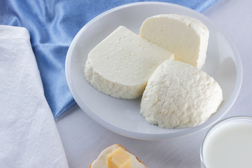 Cheese, dairy assortment on a white background, sandwich with soft cheese on a blue napkin, wooden background, wooden cutlery, white cheese on a white plate, kefir in a glass, art