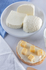 Cheese, dairy assortment on a white background, sandwich with soft cheese on a blue napkin, wooden background, wooden cutlery, white cheese on a white plate, kefir in a glass, art