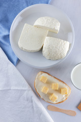 Cheese, dairy assortment on a white background, sandwich with soft cheese on a blue napkin, wooden background, wooden cutlery, white cheese on a white plate, kefir in a glass, art