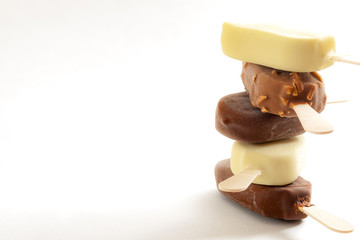 Refreshing summer food, icy cold dessert and frozen snack concept with close up on stack of sweet ice cream bars coated in milk chocolate and hazelnut on stick isolated on white with copy space