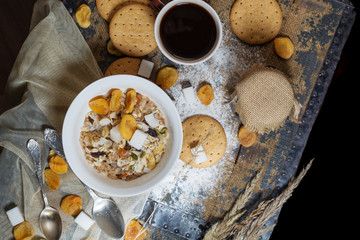 Flat lay of a rustic style breakfast with cereal, dried fruits, coffee and cookies on a wooden table, space for your text