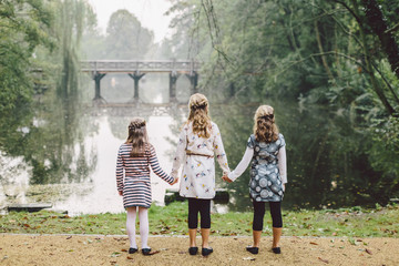 Naklejka na ściany i meble three little girls walk in park with lake view