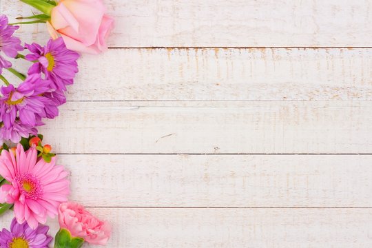 Side border of pink and purple flowers with rose, carnation and daisies against a white wood background. Copy space.