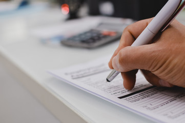 Closeup of hand writing filling job or service application form over light desk background. Signing with pen checklist, college student or education university program certificate. Business contract