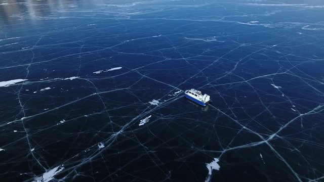 Khivus ship boat an air cushion rides to high mountains. Blue Transparent Ice field Lake Baikal reflection river. Picturesque cracks. Russia North. Tourist attraction. Winter sunny. Aerial near boat