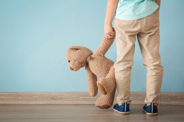 Lonely little girl with teddy bear near color wall. Autism concept