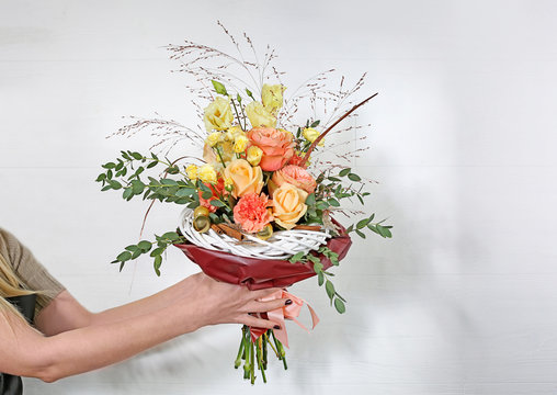 Young florist holding beautiful bouquet on white wall background