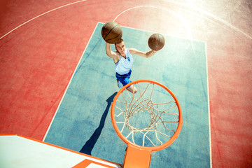 Young man jumping and making a fantastic slam dunk playing streetball, basketball. Urban authentic.