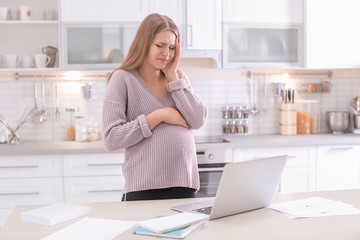 Young pregnant woman suffering from headache in home office