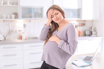 Young pregnant woman suffering from headache in home office