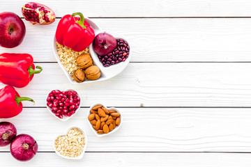 Diet for healthy heart. Food with antioxidants. Vegetables, fruits, nuts in heart shaped bowl on white wooden background top view copy space